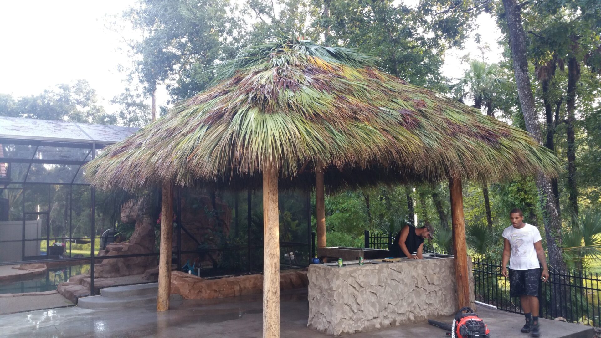 A man is working on a tiki hut at a zoo.
