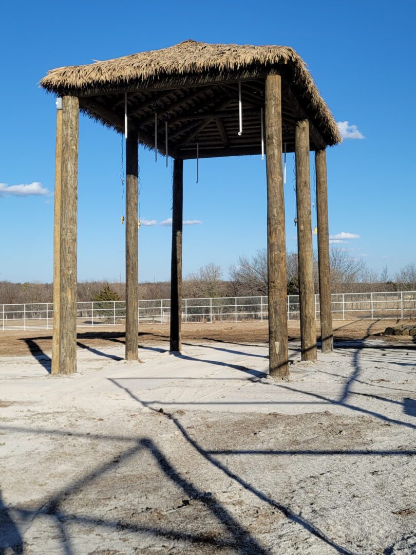 A gazebo with a thatched roof in the middle of a dirt field.