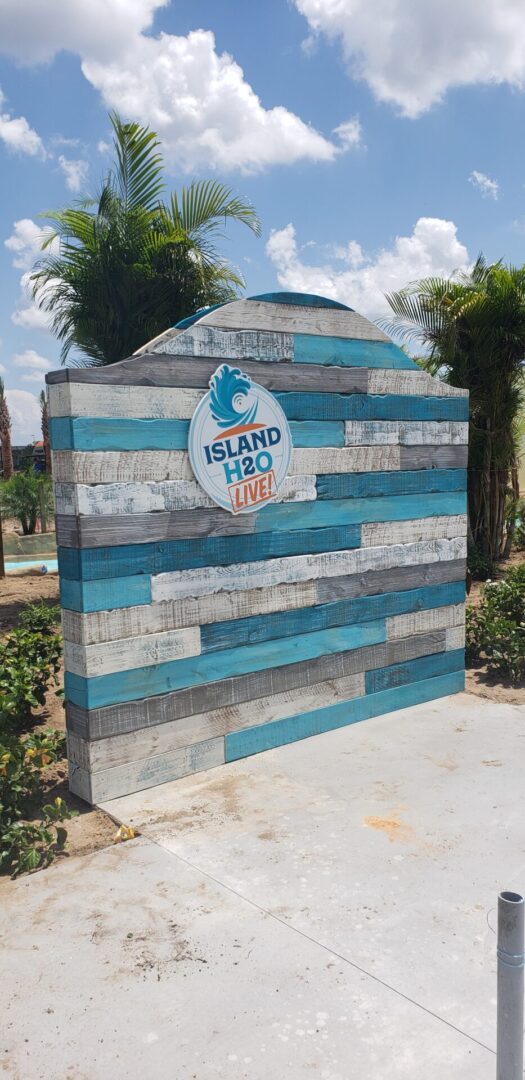 A sign with a blue sign and palm trees in front of it.