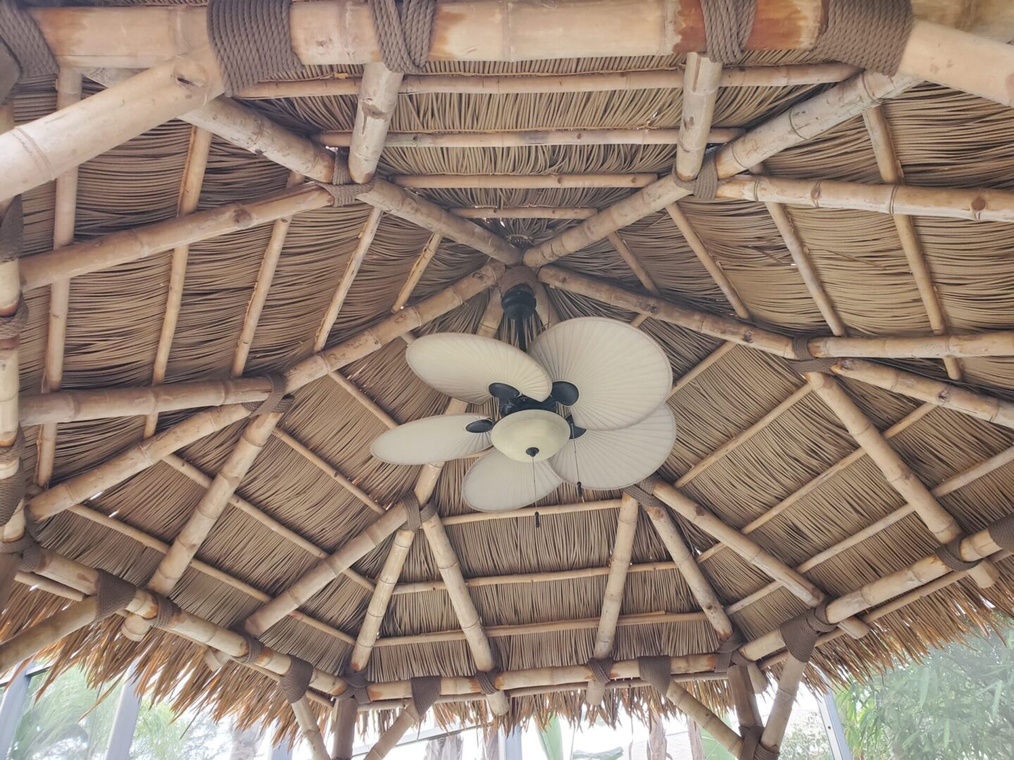 The ceiling of a tiki hut with a fan.