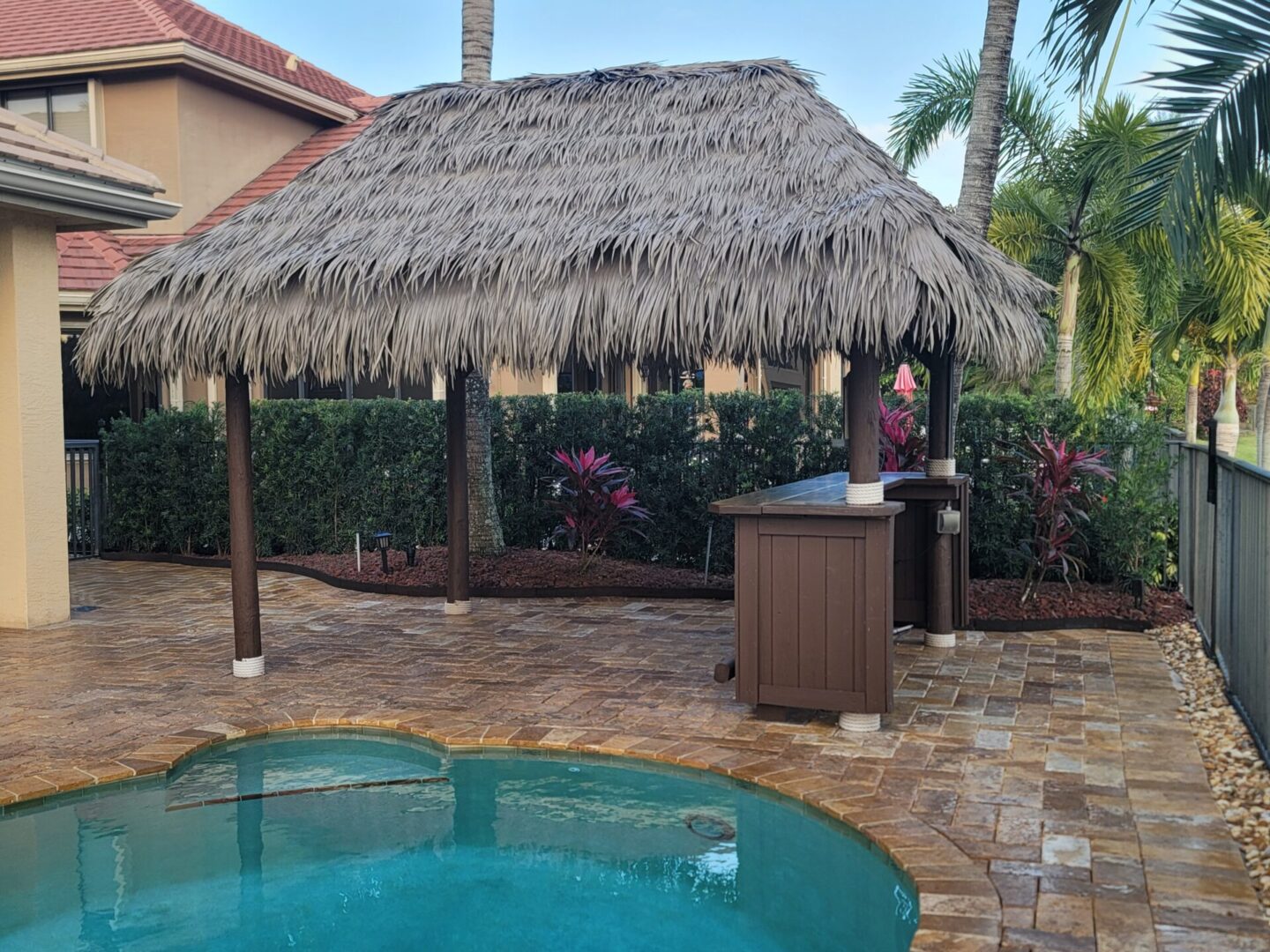 A thatched gazebo with a pool and palm trees.
