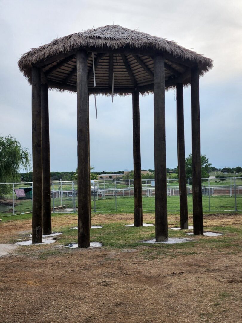 A gazebo with a thatched roof in the middle of a field.