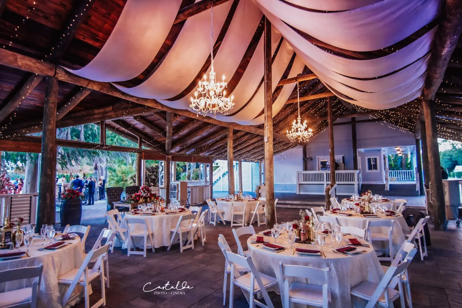 A wedding reception in a barn with white tablecloths and chandeliers.