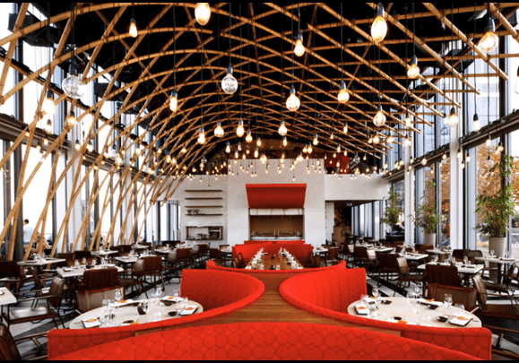 The interior of a restaurant with red chairs and tables.