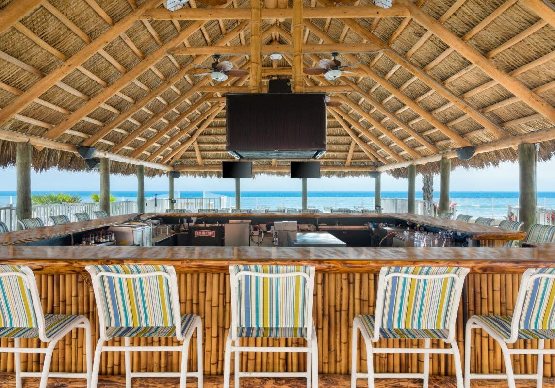 A beach bar with chairs and a view of the ocean.