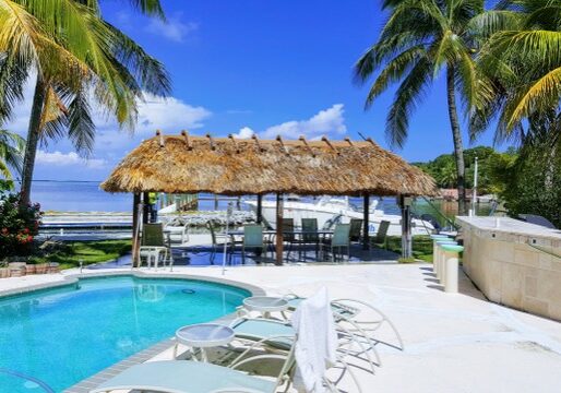 A pool with a thatched hut and palm trees.