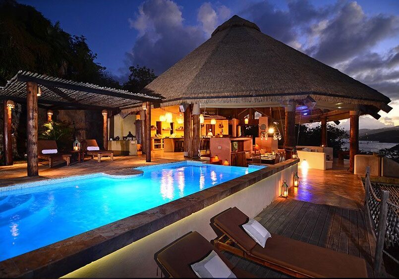 A house with a pool and lounge chairs at dusk.